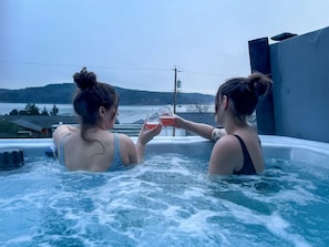 Deux personnes dans un bain à remous, avec vue sur une étendue d’eau et des collines en arrière-plan.