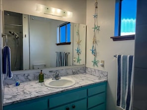 Une salle de bain avec un lavabo en marbre, des meubles de couleur turquoise, un grand miroir, des étoiles de mer décoratives sur le mur et une fenêtre avec vue.