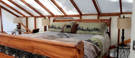 Un dormitorio con cama de madera, tragaluz, una mesita pequeña y una mesita de noche.