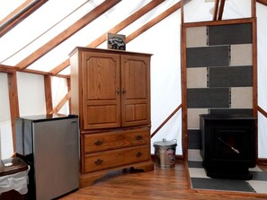 A wooden cabinet with drawers, a black stove, and a refrigerator in a room with wooden beams and a tiled wall.