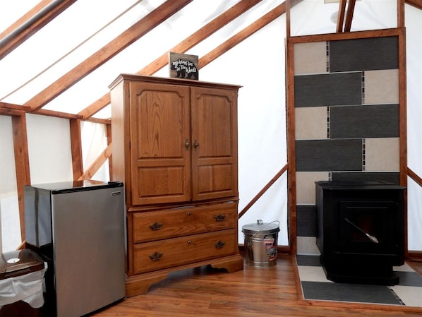 A wooden cabinet with drawers, a black stove, and a refrigerator in a room with wooden beams and a tiled wall.