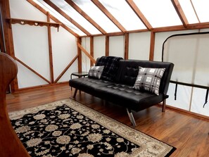 A loft-style room with a black leather sofa, patterned rug, wooden beams, and a skylight.