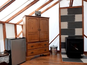 A wooden cabinet with drawers, a black stove, and a refrigerator in a room with wooden beams and a tiled wall.