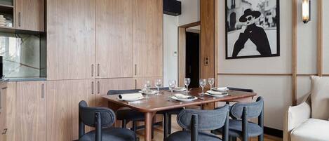 Un espace repas moderne avec une table en bois dressée pour quatre personnes, entourée de chaises aux couleurs sombres.