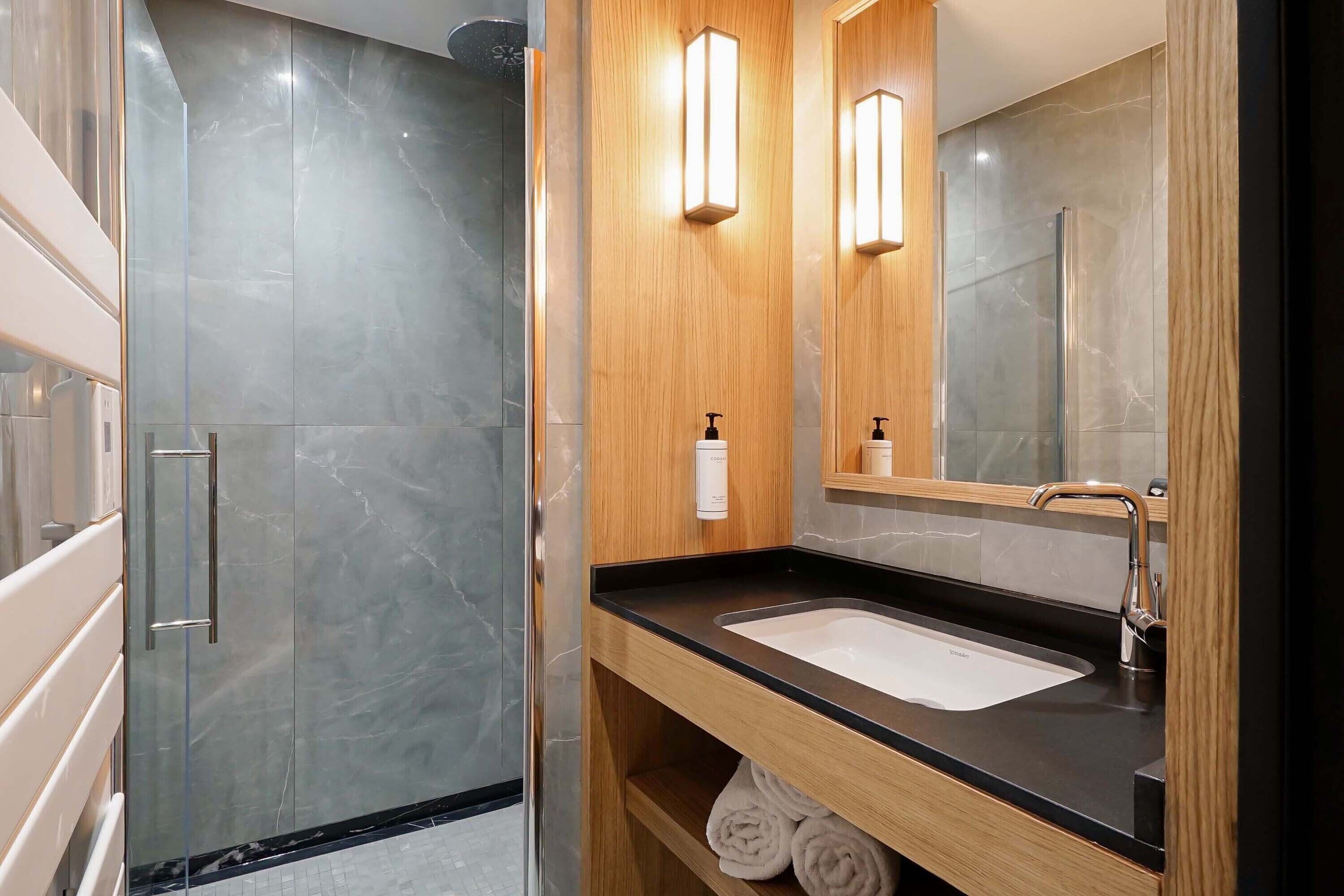 A modern bathroom with a glass shower enclosure, a wooden vanity with a black countertop, and a large mirror.