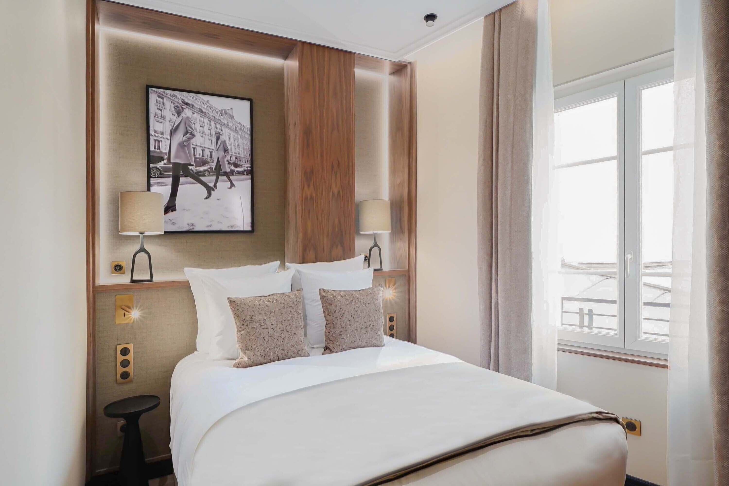 A hotel room with a large bed, two bedside tables with lamps, a framed picture on the wall, and a window with curtains.