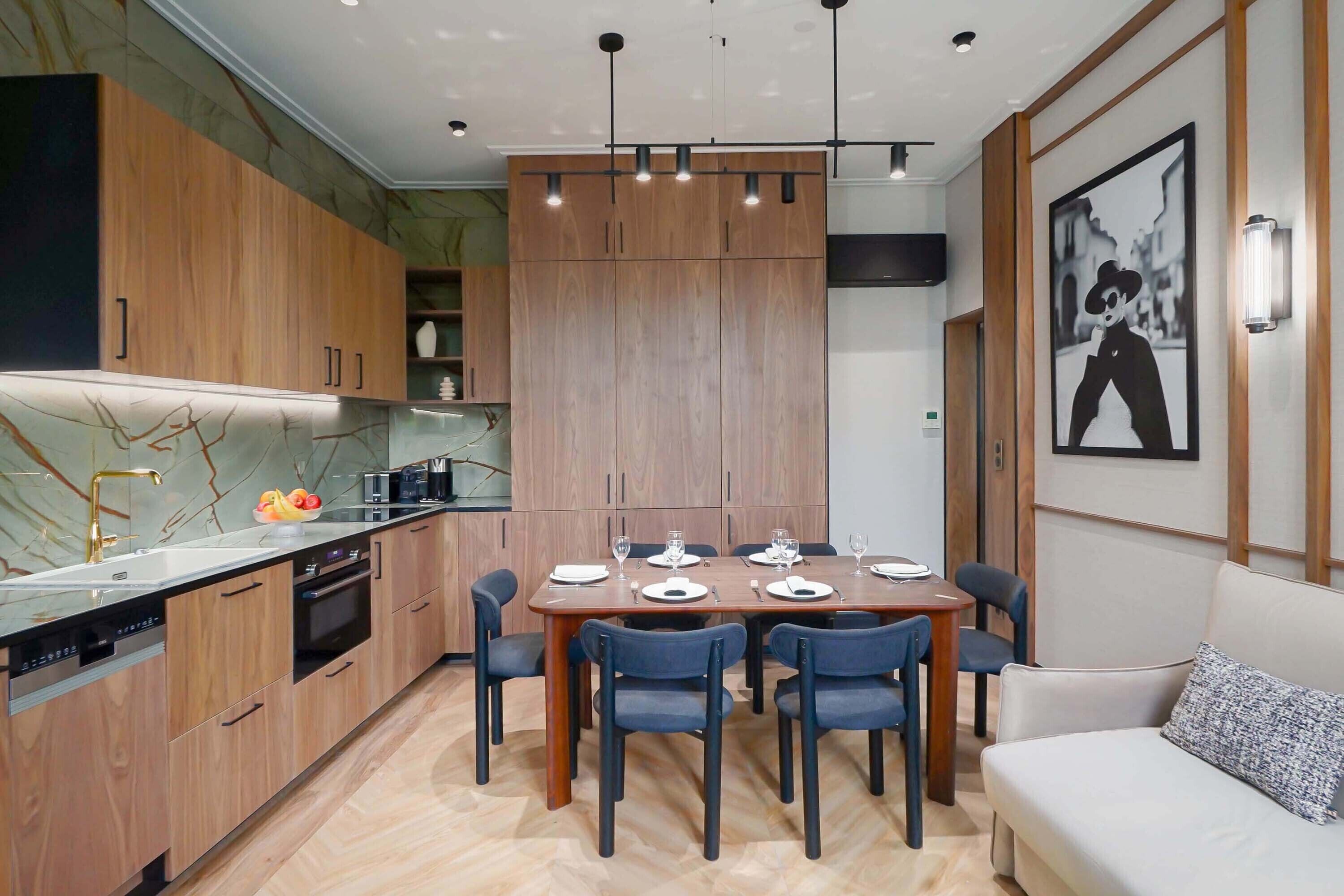 A modern kitchen with wooden cabinets, a marble countertop, and a dining area with a table set for six.