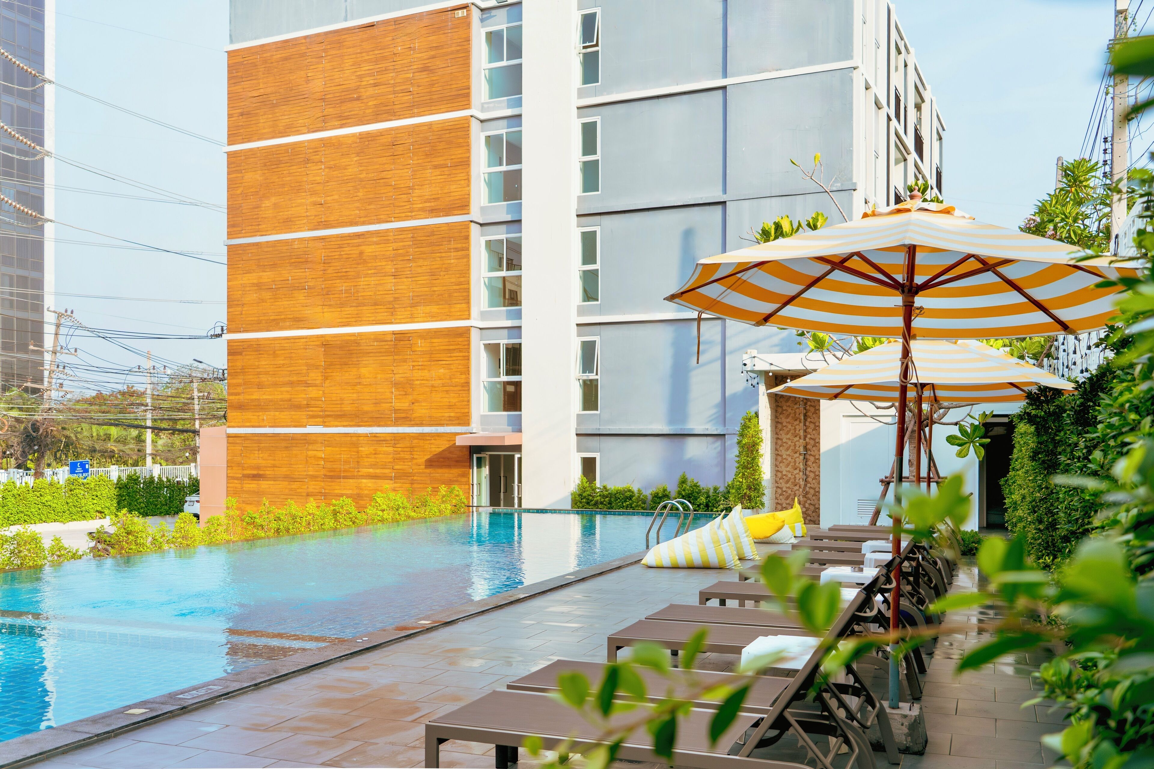 A modern building with a swimming pool, outdoor seating, and umbrellas.