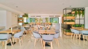 Een moderne eetruimte met meerdere tafels en stoelen, een groot raam met uitzicht en een verticale plantenwand.