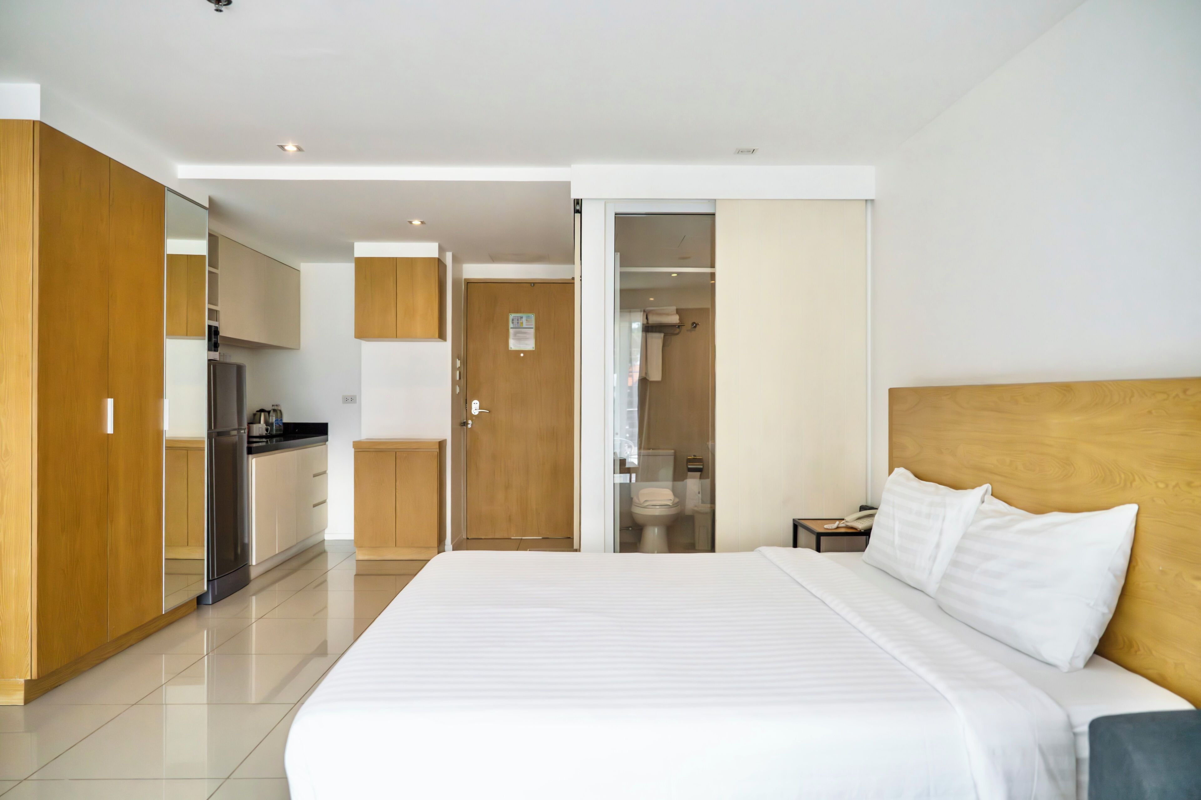 Una camera d'albergo moderna con un letto grande, una testiera in legno, un piccolo comodino e vista sulla zona cucina.