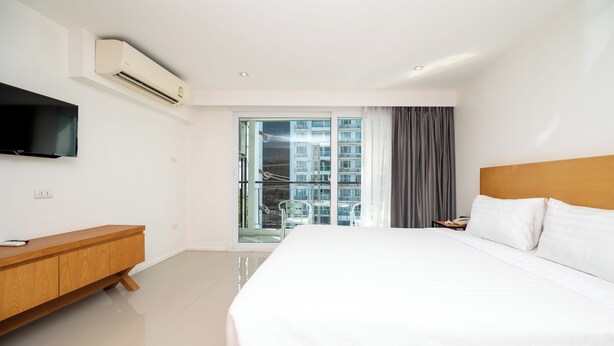 A modern hotel room with a large bed, a wooden bedside table, a flat-screen TV, and a balcony with a city view. - Fourium Pattaya Hotel and Serviced Residence (Pattaya)