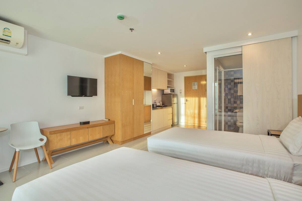 Une chambre d’hôtel moderne équipée de deux lits, d’un bureau, d’une chaise, d’une télévision et d’une kitchenette.