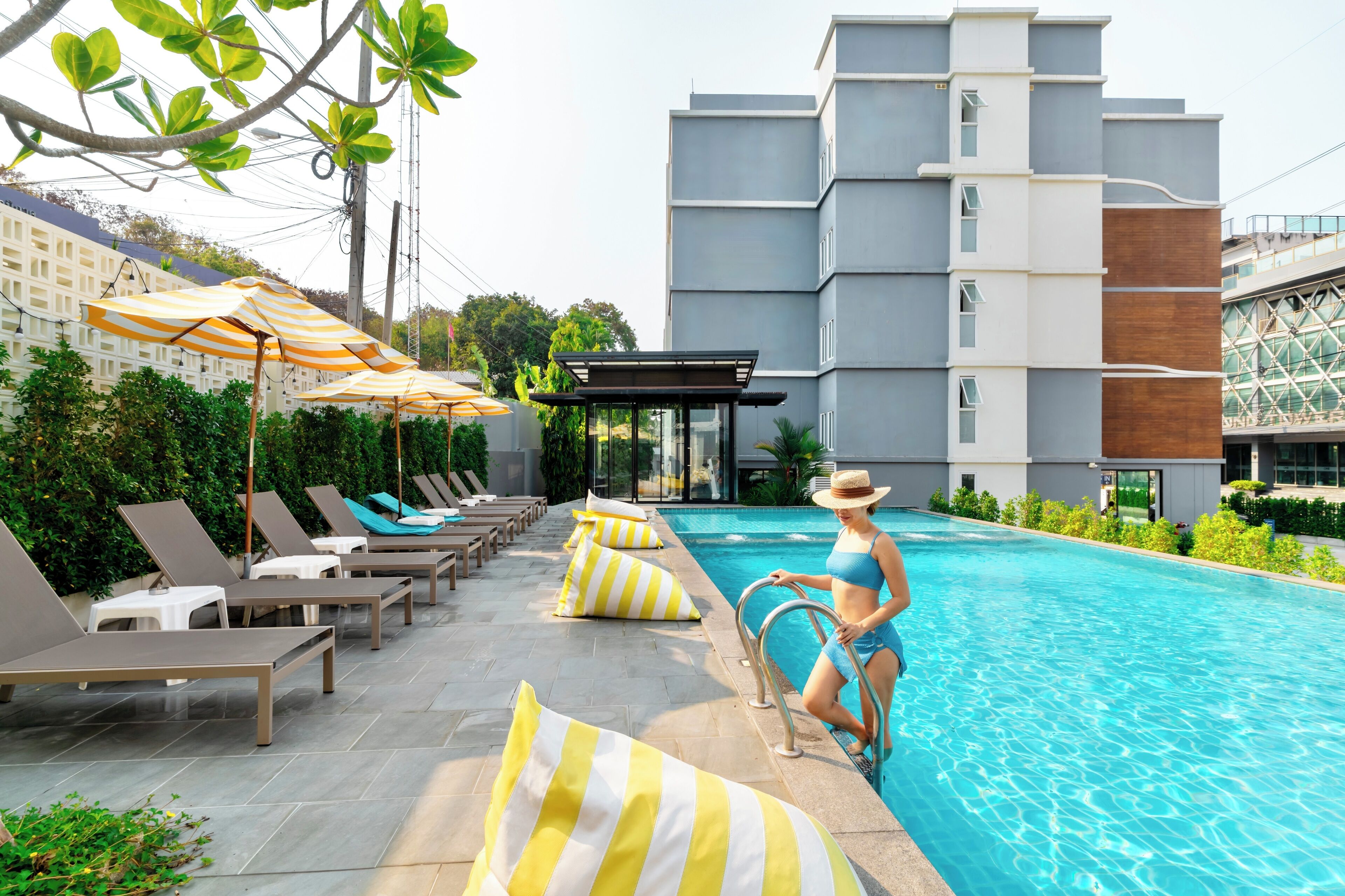 A swimming pool area with lounge chairs and umbrellas, a covered seating area, and a modern building in the background.