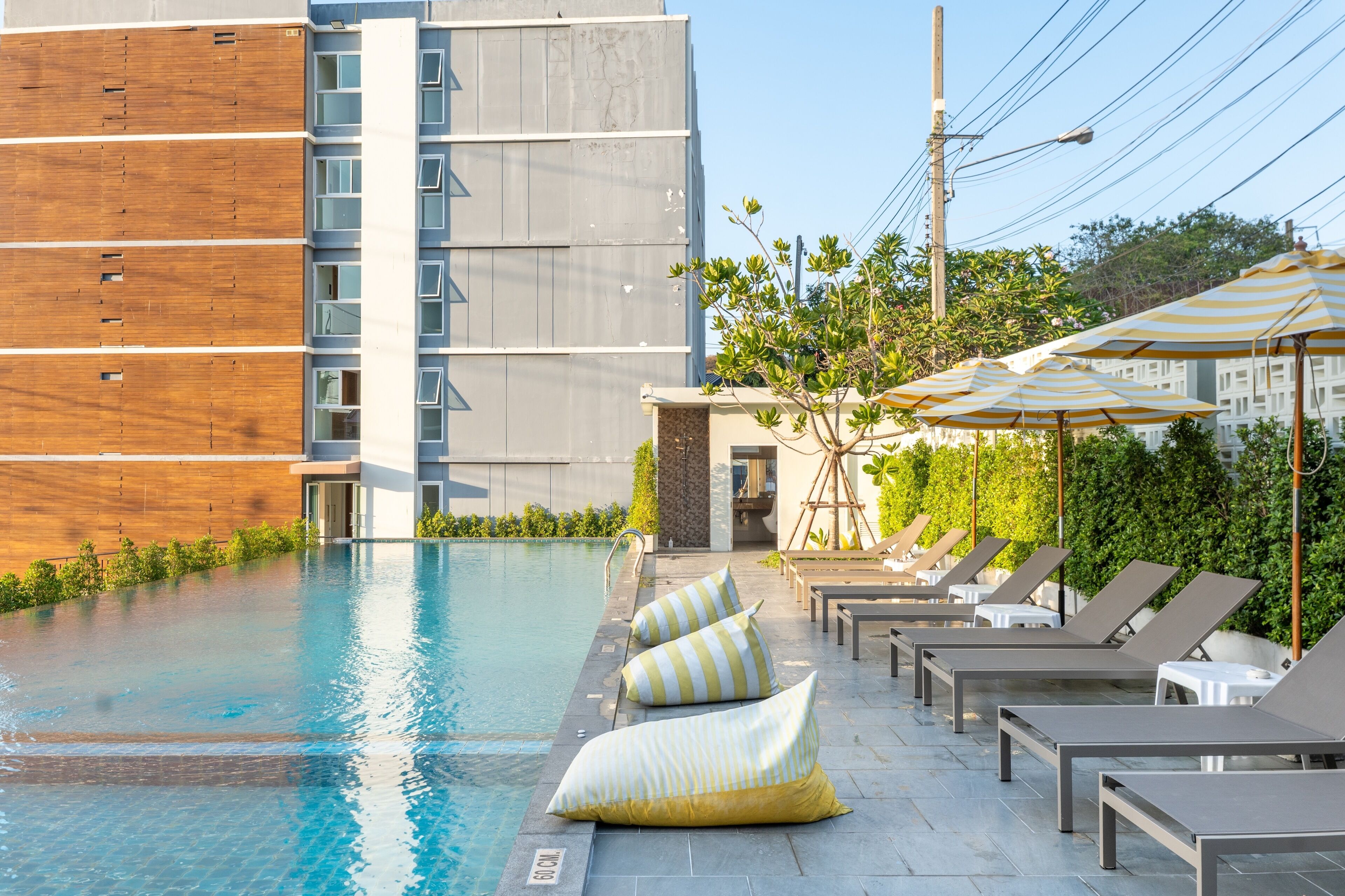 A swimming pool with lounge chairs and umbrellas, surrounded by greenery and a modern building.