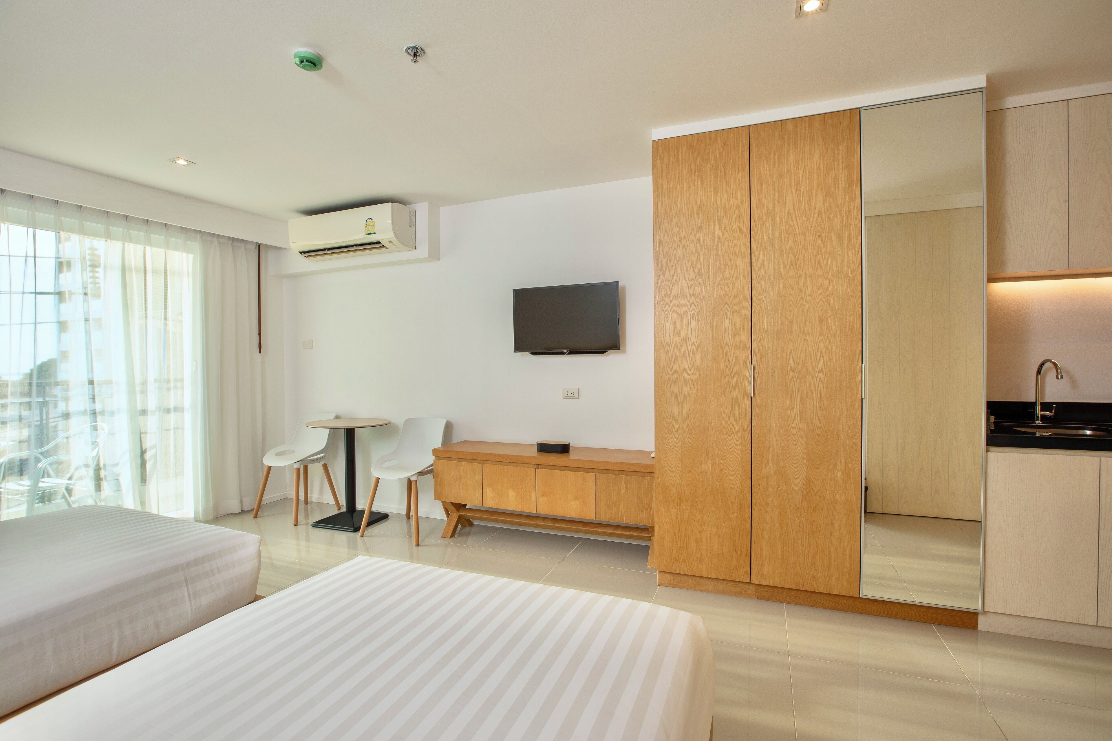 Ein modernes Hotelzimmer mit zwei Betten, einem Schreibtisch, einem Fernseher und einer Küchenzeile.