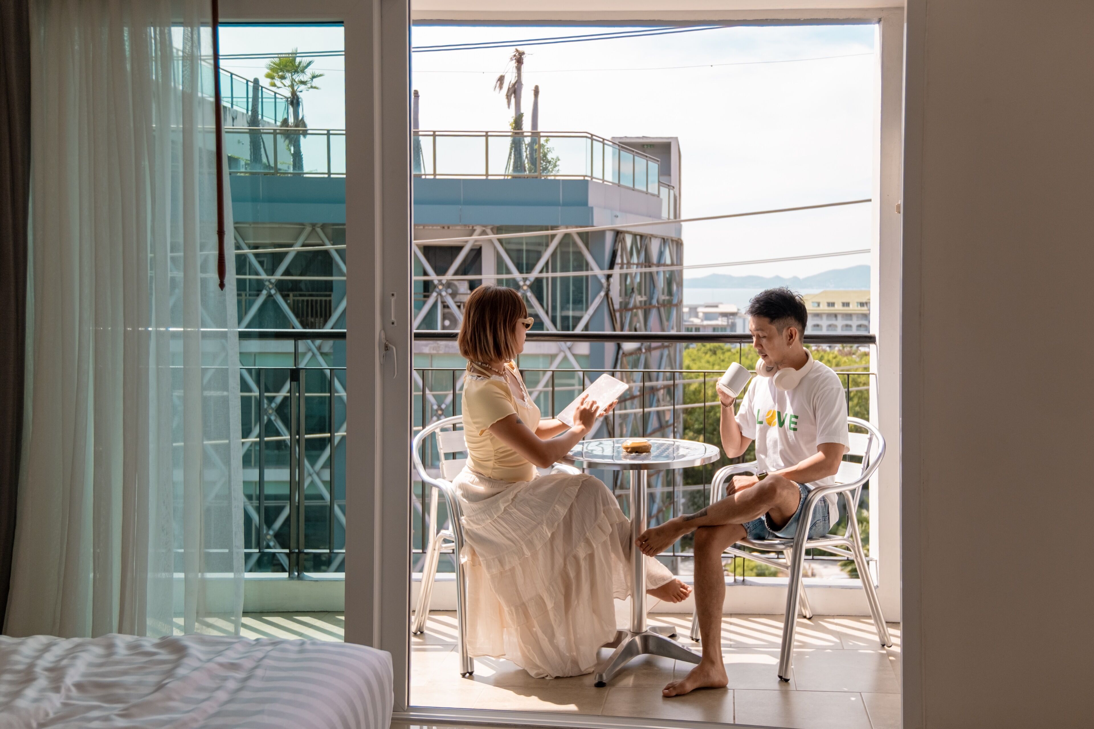 A balcony with a glass door, a bed, and a table with two people seated.