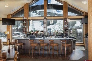 Een bar met een groot raam dat uitzicht biedt op een besneeerd berglandschap.