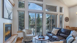 A spacious living room with a fireplace, large windows, a leather sofa, and a striped armchair. - Alpenglow - Ski-In/Out Durango Condo with Hot Tub (Durango)