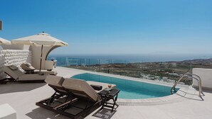 Ein Pool auf dem Dach mit Liegestühlen und Geländer aus Glas mit Blick auf eine Küstenlandschaft.