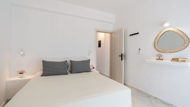 Ein Schlafzimmer mit einem Bett, zwei Nachttischen, einem Regal, einem an der Wand befestigten Spiegel, einer Tür und einem Regal mit Dekoration.