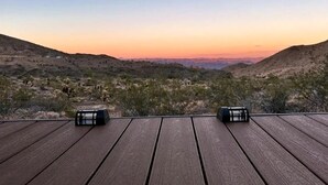 A wooden deck with two black objects, likely speakers, overlooking a hilly landscape with sparse vegetation.