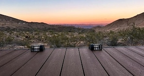 A wooden deck with two black objects, likely speakers, overlooking a hilly landscape with sparse vegetation.