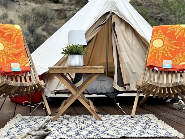 A tent with a table and chairs, a small plant, and a rug on a wooden deck.