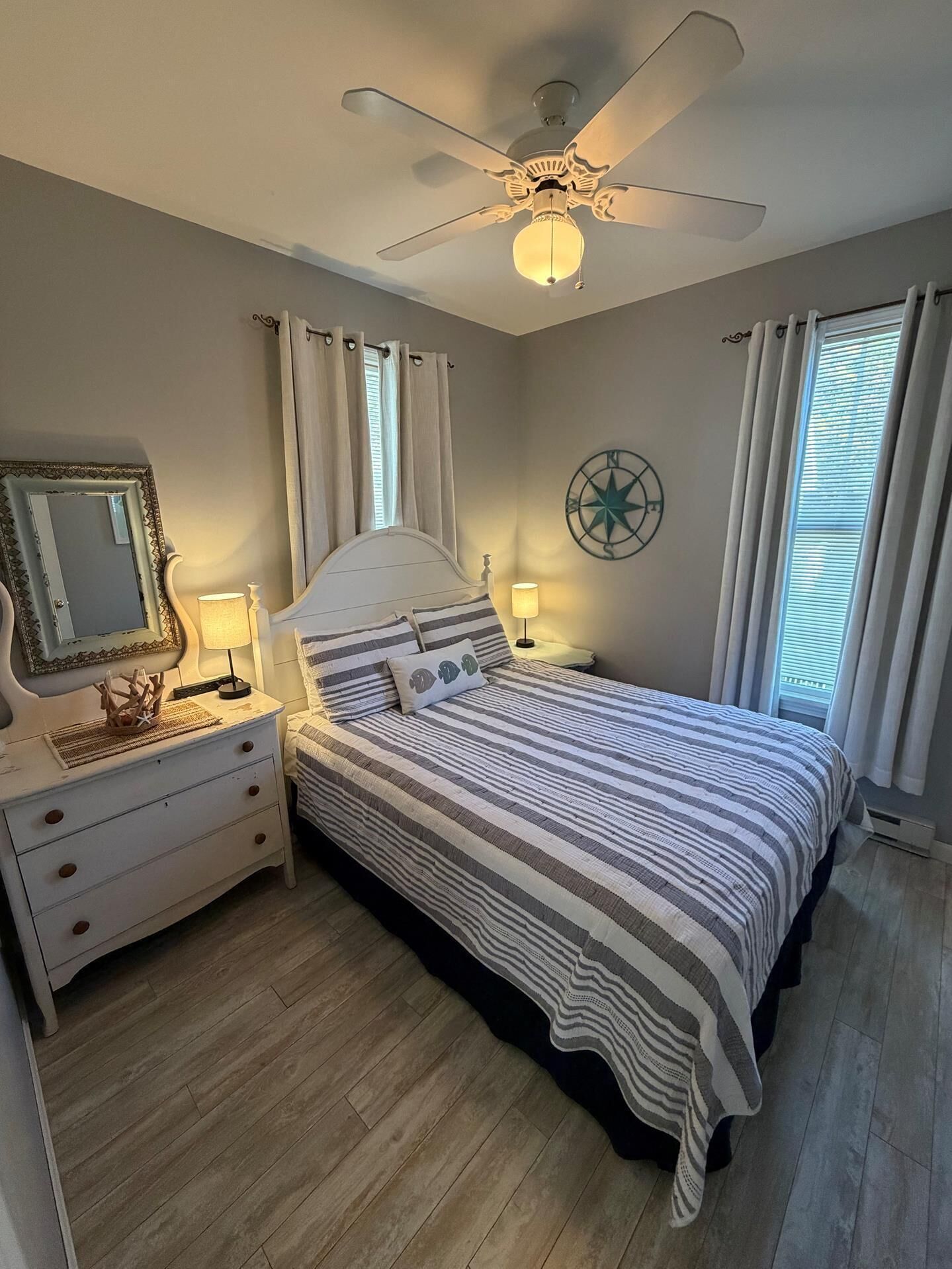 A bedroom with a bed, nightstands, a ceiling fan, a wall clock, and a window with curtains.