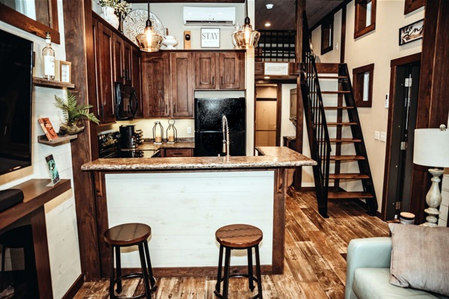 A kitchen with wooden cabinets, a central island with stools, a refrigerator, and a staircase.