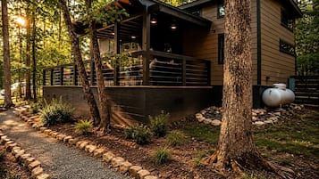 A modern house with a covered porch, surrounded by trees and a gravel path.