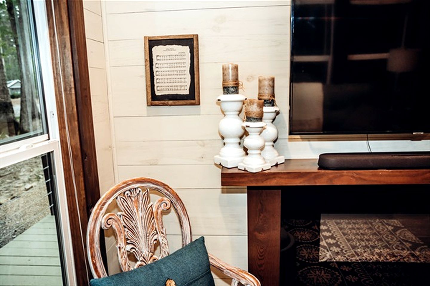 A room with a wooden chair, a framed paper on the wall, and a table with candles.