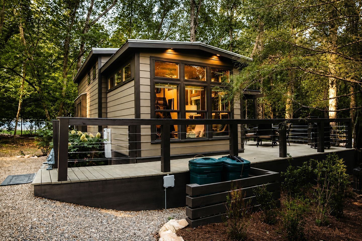 A modern cabin with a deck, surrounded by trees.