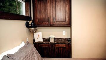 A bedroom with a bed, a nightstand, a wooden cabinet above the nightstand, and a window with a view of trees.