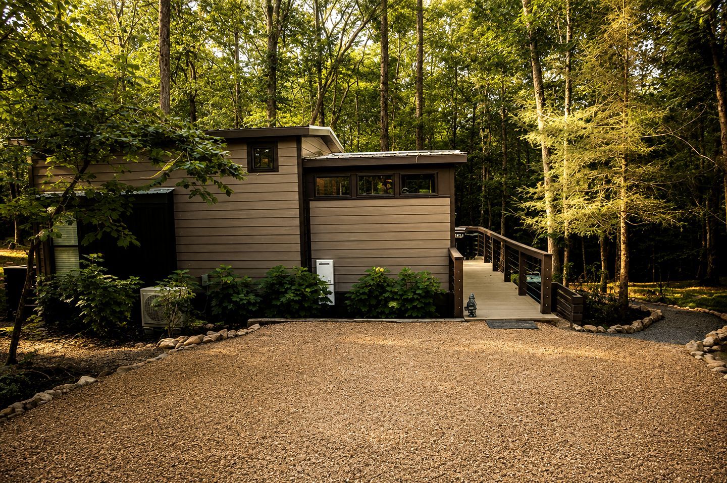 A modern house with a gravel driveway, surrounded by trees.