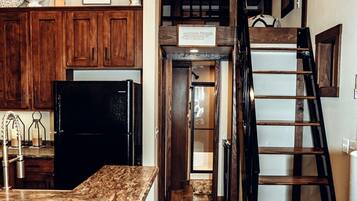 A kitchen with wooden cabinets, a black refrigerator, a marble countertop, a ladder, and a sign above the door.
