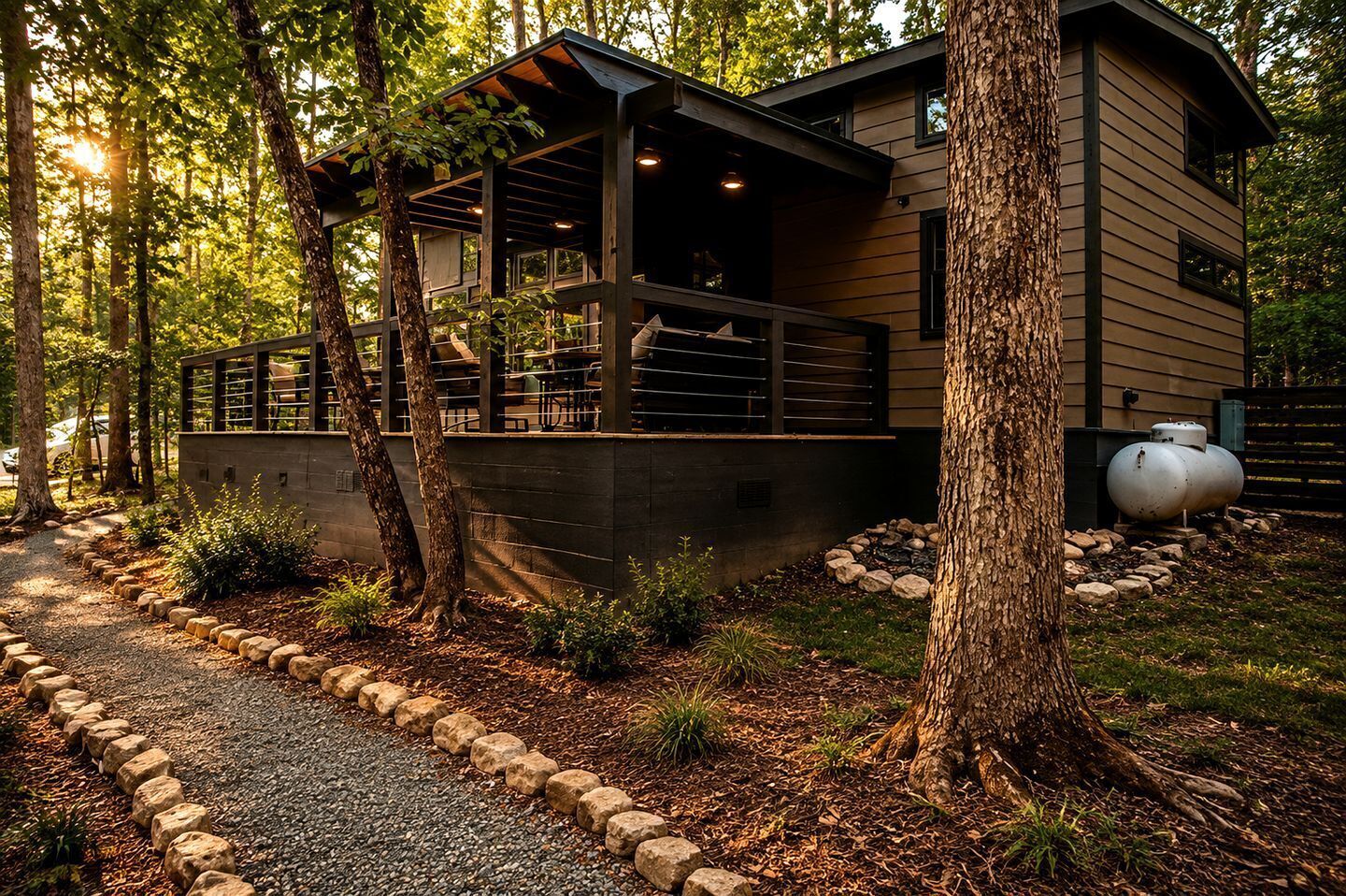 A modern house with a covered porch, surrounded by trees and a gravel path.