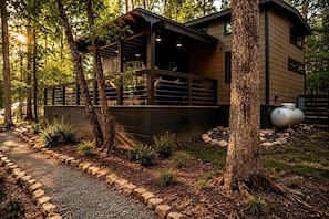 A modern house with a covered porch, surrounded by trees and a gravel path. - Leprechaun Lodge at The Retreat at Deer Lick Falls in Tennessee (Monteagle)