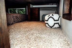 Una habitación compacta con piso alfombrado, una cama con cubrecolor marrón y un almohadón blanco con diseño geométrico negro.