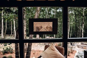 A framed artwork of mountains with the text 'THE MOUNTAINS ARE CALLING AND I HEAR THEM' in a room with a view of a forest. - Leprechaun Lodge at The Retreat at Deer Lick Falls in Tennessee (Monteagle)