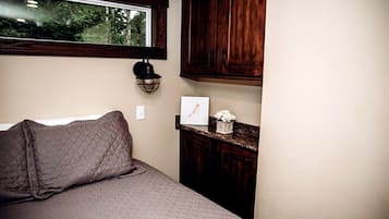 A bedroom with a bed, a window, wooden cabinets, and a small table with a picture and flowers.