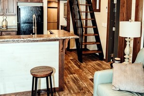A kitchen with a marble countertop, a wooden stool, and a staircase leading to another room. - Leprechaun Lodge at The Retreat at Deer Lick Falls in Tennessee (Monteagle)