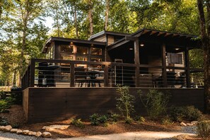 A modern wooden house with a covered patio, surrounded by trees. - Leprechaun Lodge at The Retreat at Deer Lick Falls in Tennessee (Monteagle)
