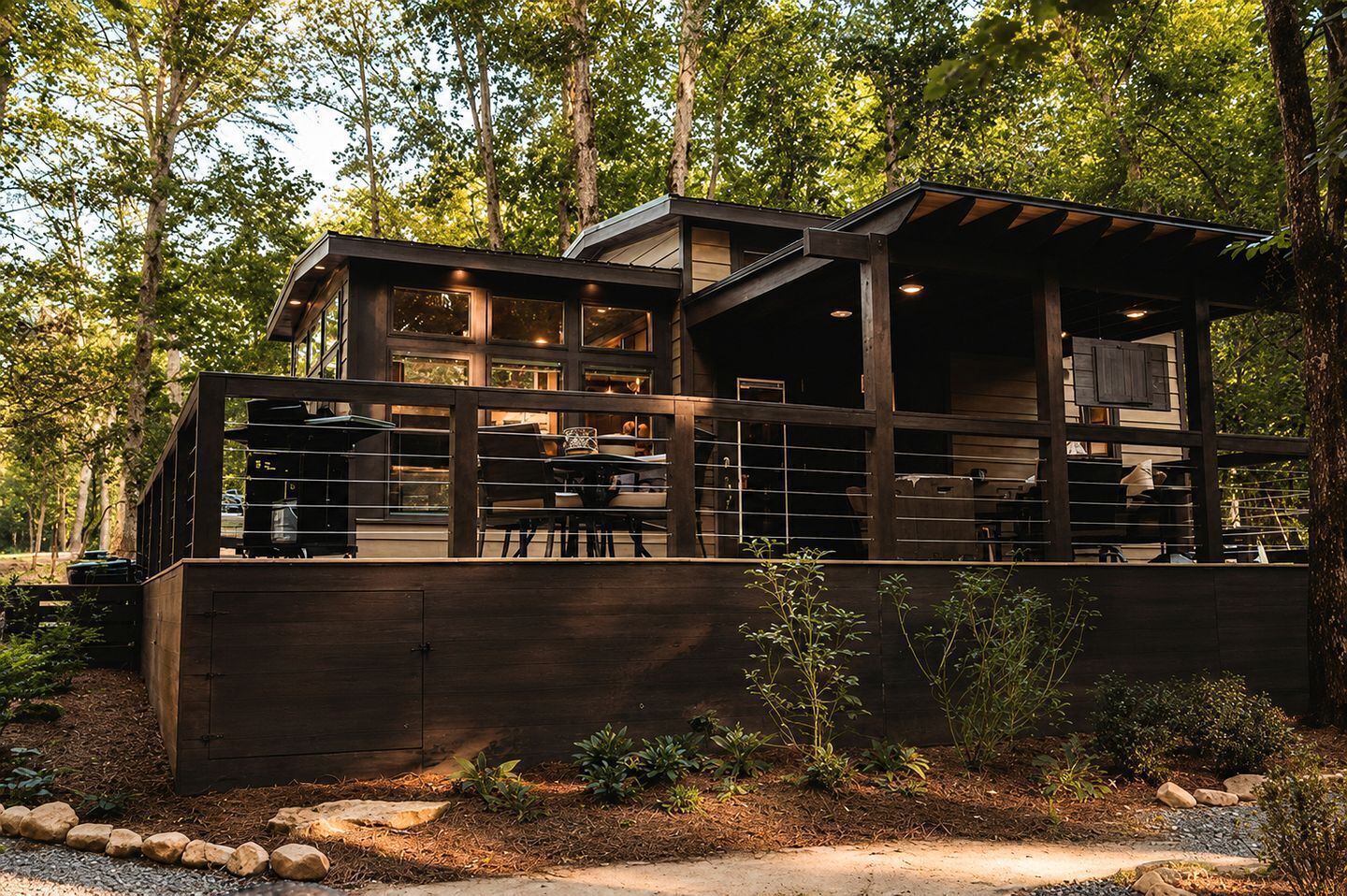 A modern wooden house with a covered patio, surrounded by trees.