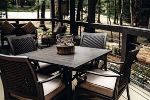 An outdoor patio with a table and chairs, surrounded by a wooden deck and a view of trees. - Leprechaun Lodge at The Retreat at Deer Lick Falls in Tennessee (Monteagle)