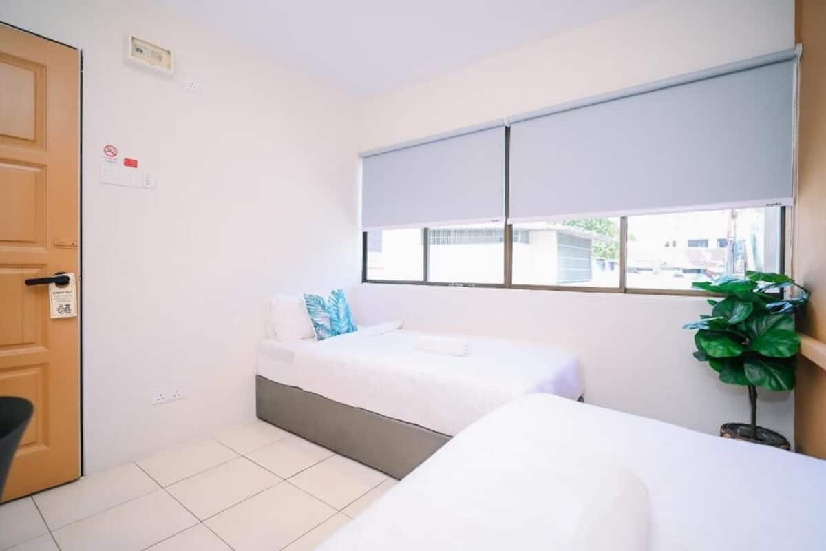 Una habitación de hotel con una cama, una silla, un ventanal con persianas, una planta en maceta y una puerta.