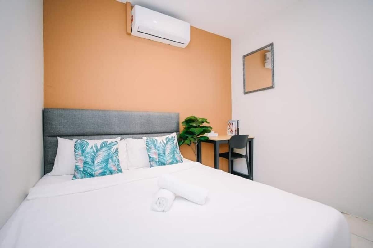Habitación de hotel con cama, aire acondicionado, escritorio, una silla y una planta en maceta.