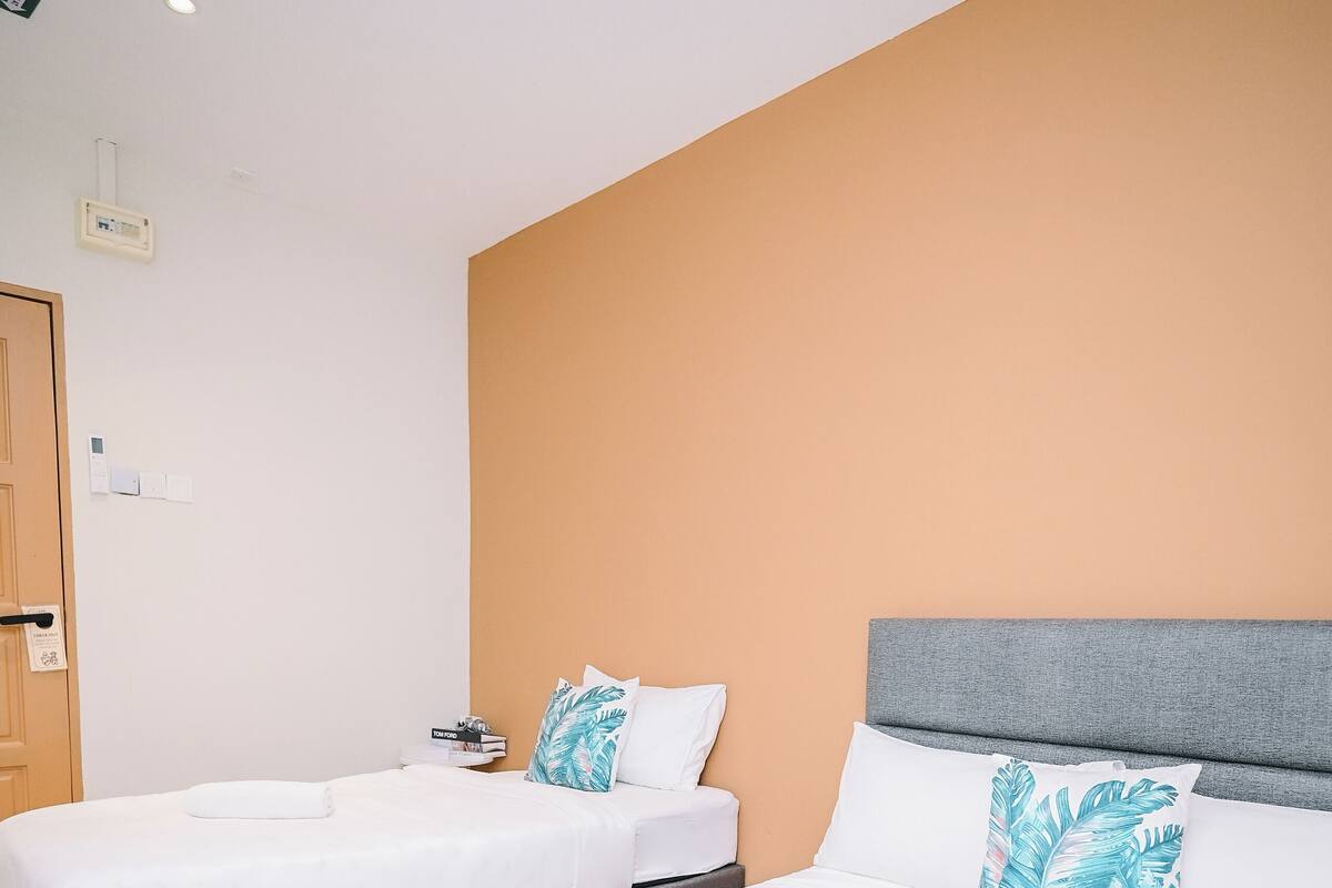 Una habitación de hotel con dos camas, ropa de cama blanca y un cabecero gris.