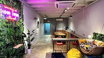Un interior moderno con una hamaca colgante, un letrero de neón, una zona de bar y un área de descanso con sillones tipo bean bag.