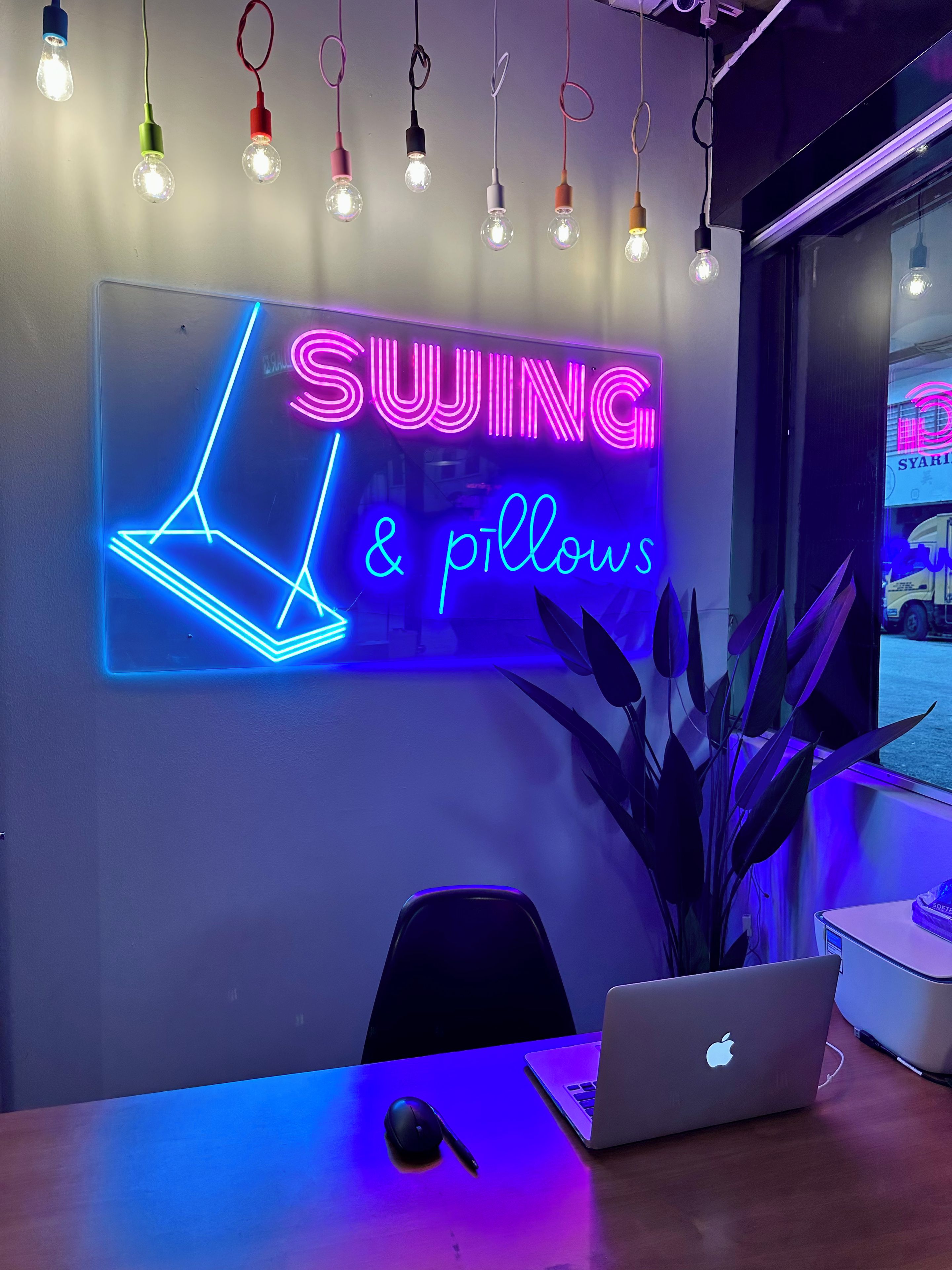Una habitación con un letrero de neón que dice 'SWING & pillows' y una computadora portátil sobre una mesa.