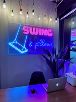 Una habitación con un letrero de neón que dice 'SWING & pillows' y una computadora portátil sobre una mesa.